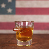 Shot glass with bullet imbedded in the side, filled with whiskey and flag in the background
