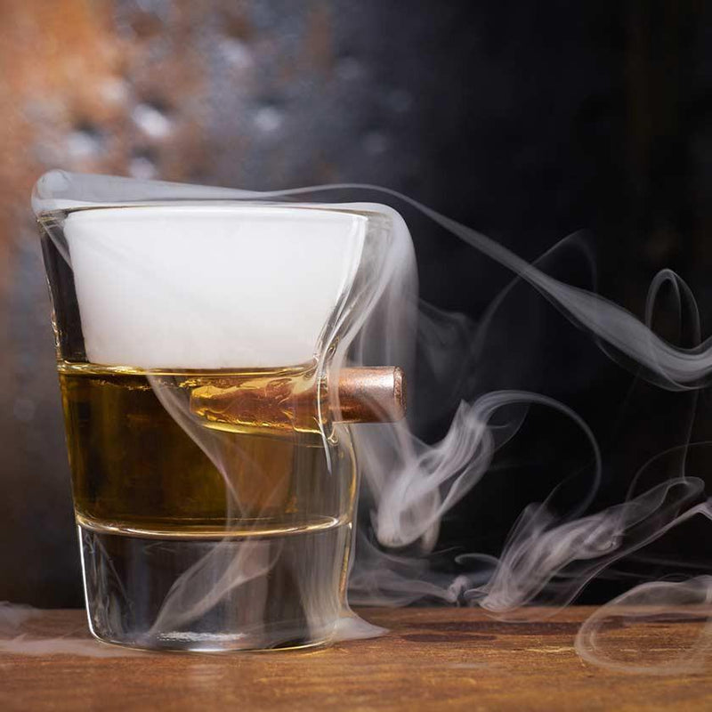 Shot glass with bullet imbedded in the side, filled with whiskey and smoke bellowing over the glass