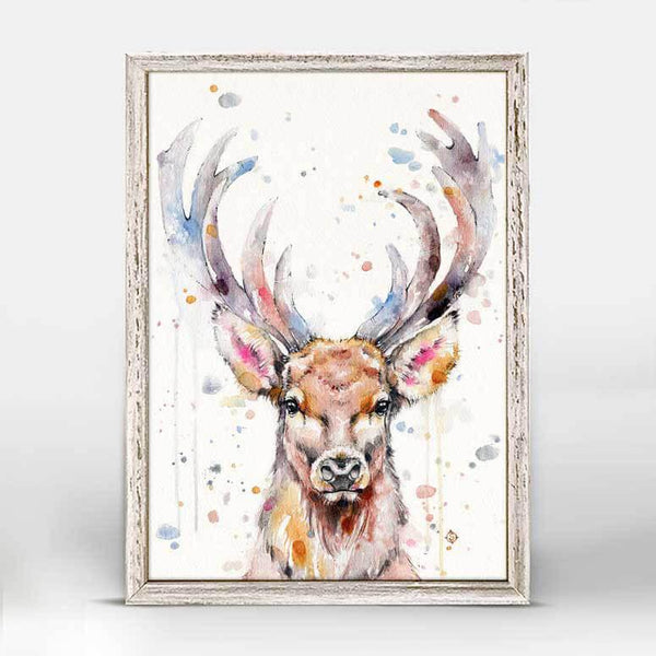 The bust of a brown male deer with full grown antlers faces forward with a spray of pastel watercolor splashes and spots in the foreground.