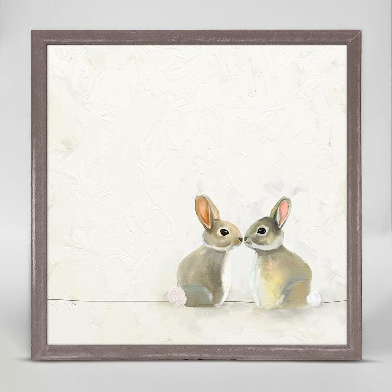 A print in color of two baby bunnies sitting nose to nose in front of a cream-colored wall.