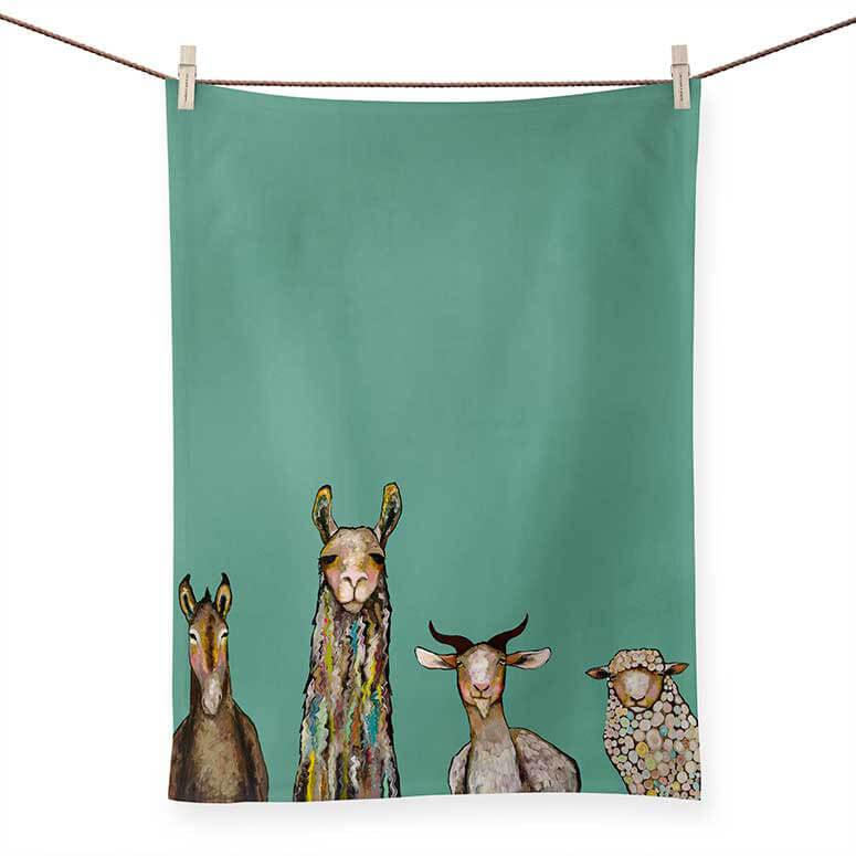 A tea towel with a dark teal background displays a donkey, llama, goat and a sheep painted in various colors  and styles facing forward.